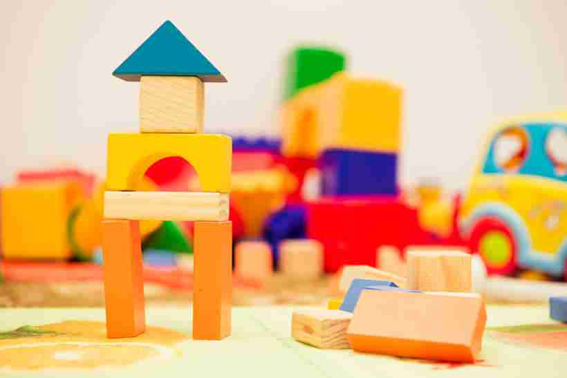 Colorful wooden toy building block structure with more colorful blurry wooden blocks and other toys in the background
